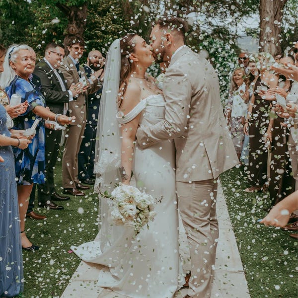 image of  couple sharing a kiss under a shower of confetti and surrounded by their guests 