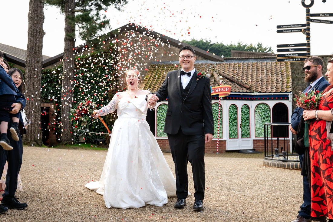 A couple holding hands being showered with red confetti 